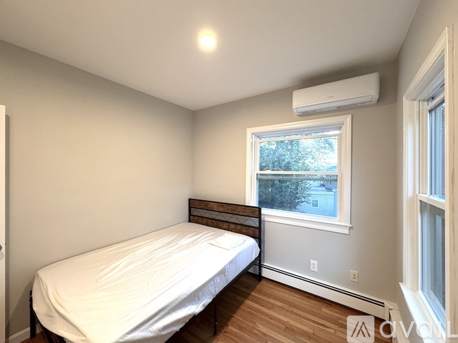 A bedroom with a bed, a window, and a wall-mounted air conditioner.