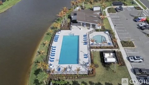 An aerial view of a pool surrounded by a parking lot and palm trees.