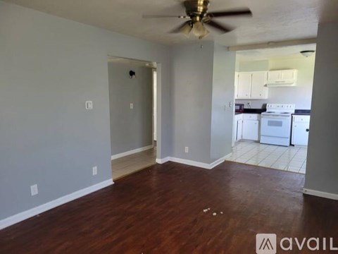 A room with a ceiling fan and a kitchen in the background.