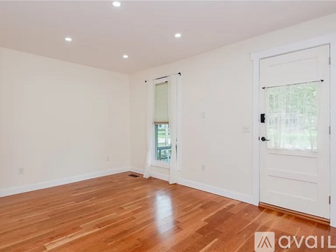 A room with wooden floors and white walls, with a door on the right side.