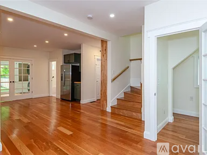 A spacious room with wooden floors and a staircase leading to another room.