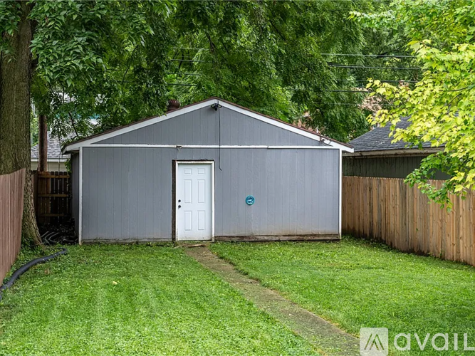A grey shed with a white door is surrounded by a green lawn and trees.