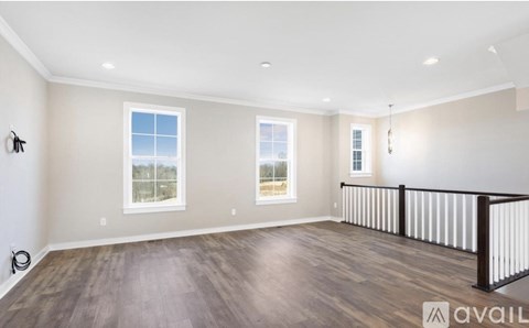 A spacious room with wooden floors and three windows.