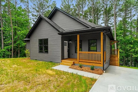 A house with a grey exterior and a wooden porch is surrounded by greenery.