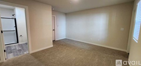 A spacious room with beige walls and carpeted floor, featuring a door and a window.