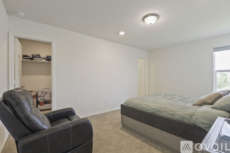 A black leather chair sits in a bedroom with a bed and a shelf.