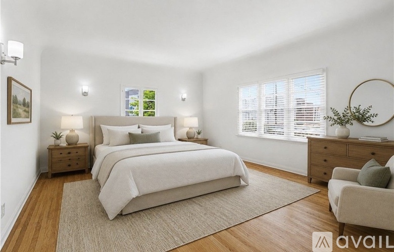 A bedroom with a large bed, a nightstand with a lamp, a chair, and a plant.