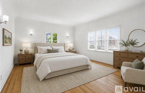 A bedroom with a large bed, a nightstand with a lamp, a chair, and a plant.
