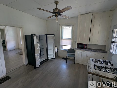 A kitchen with a black fridge, white cabinets, and a ceiling fan.