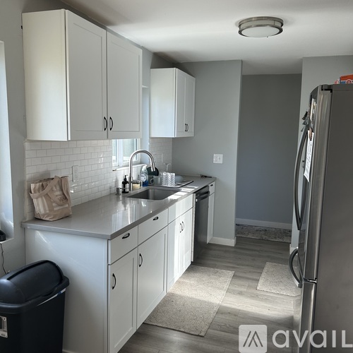 A kitchen with white cabinets and a black trash can.