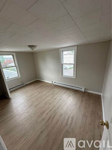 A room with wooden flooring and two windows.