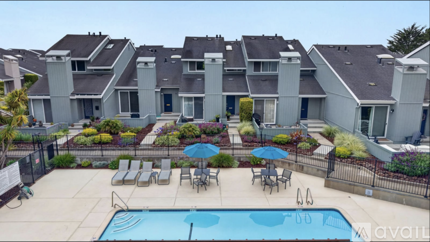 A swimming pool is surrounded by chairs and umbrellas in a residential area.
