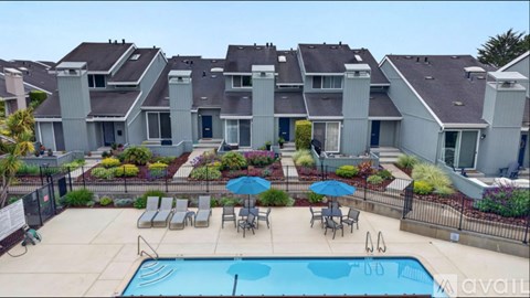 A swimming pool is surrounded by chairs and umbrellas in a residential area.