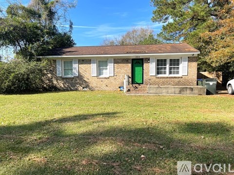 A house with a green door and white windows is surrounded by a grassy area.