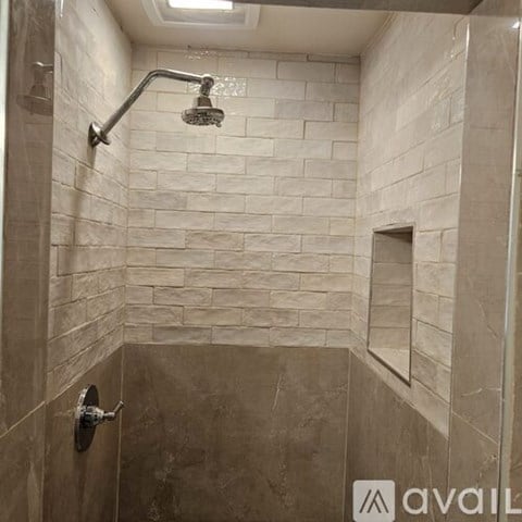 A shower area with a wall of tiles and a shower head.