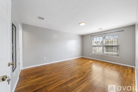 A spacious room with wooden flooring and a window with blinds.