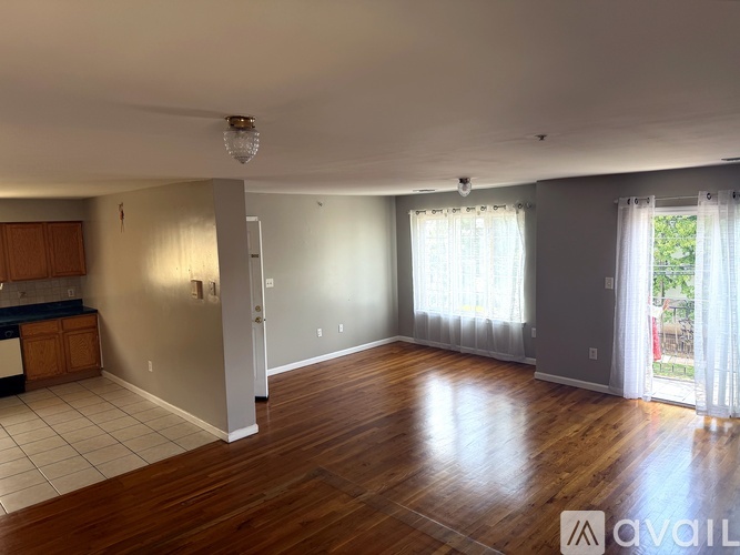 A spacious living room with hardwood floors and a kitchen area to the left.