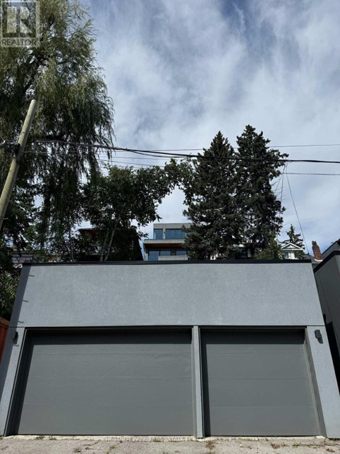 A grey garage door is closed and there is a tree in front of a building.