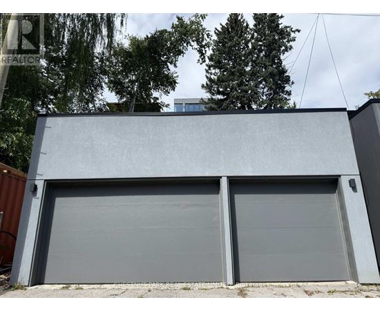 A grey garage door is closed and there is a tree in the background.