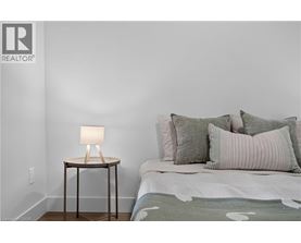 A bedroom with a bed, a lamp, and a wall with a REALTOR® logo.
