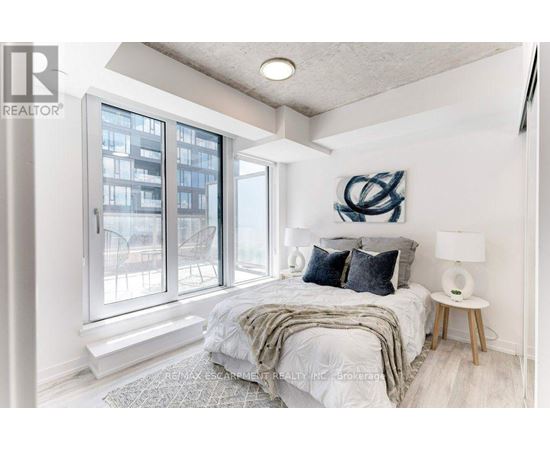 A bedroom with a large bed and a view of a building outside the window.