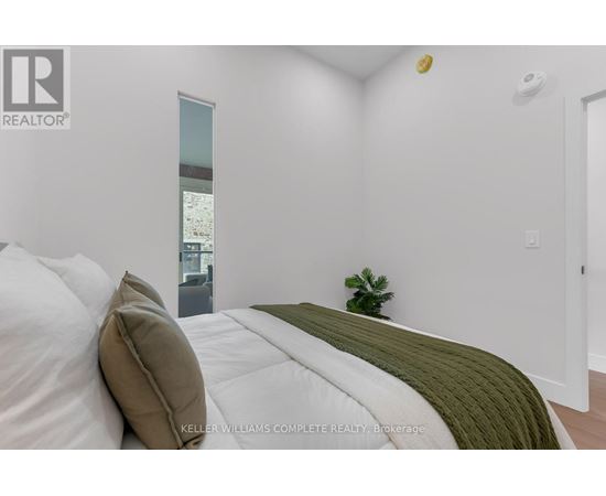 A bedroom with a bed, a side table, and a plant.