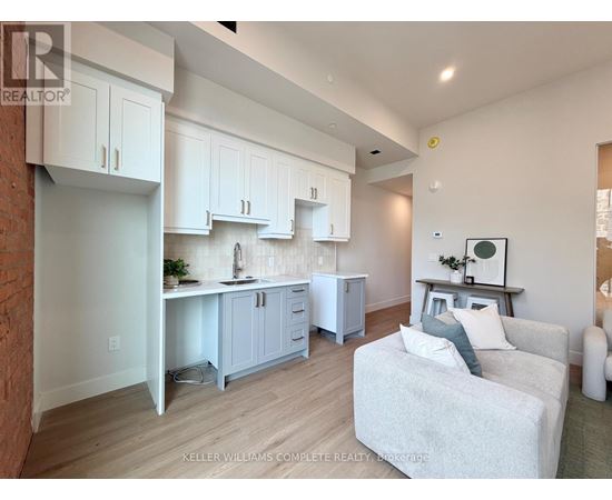 A well-lit kitchen with white cabinets and a grey couch.