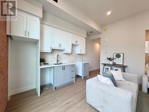 A well-lit kitchen with white cabinets and a grey couch.