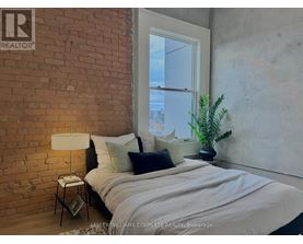 A bedroom with a brick wall and a bed with a white comforter.