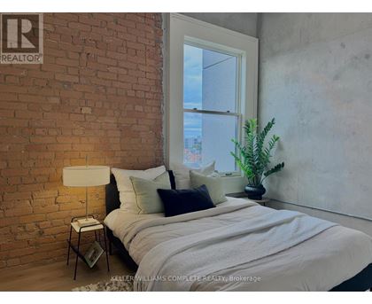A bedroom with a brick wall and a bed with a white comforter.
