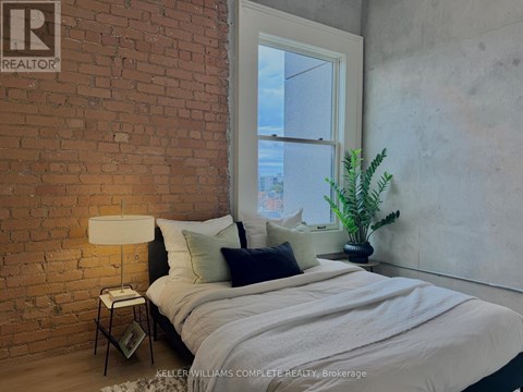 A bedroom with a brick wall and a bed with a white comforter.