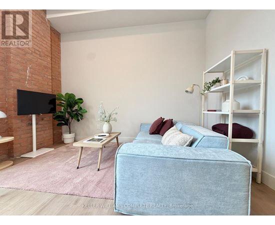 A living room with a blue couch, a white shelf, and a flat screen TV mounted on a brick wall.