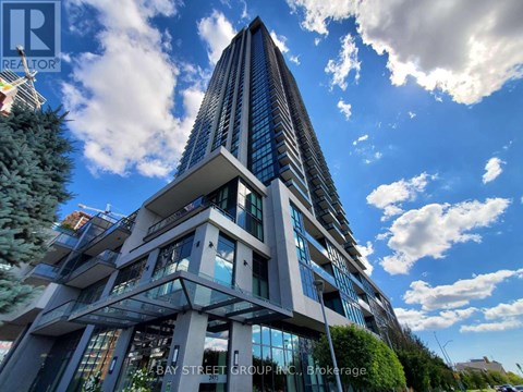 A tall, modern building with a glass facade and a unique design stands under a blue sky with clouds.
