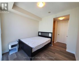 A bedroom with a bed, nightstand, and a wood floor.
