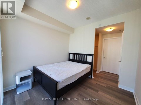 A bedroom with a bed, nightstand, and a wood floor.
