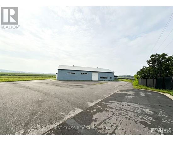 A large grey building with the words "FIRST CLASS REALTOR" on the side is situated in a spacious area with a paved road leading up to it.