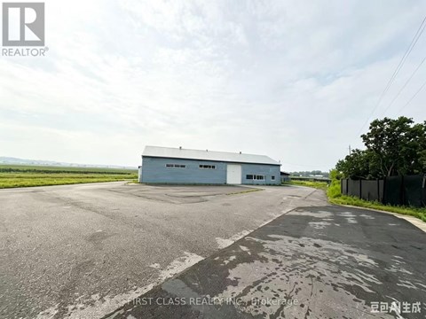 A large grey building with the words "FIRST CLASS REALTOR" on the side is situated in a spacious area with a paved road leading up to it.