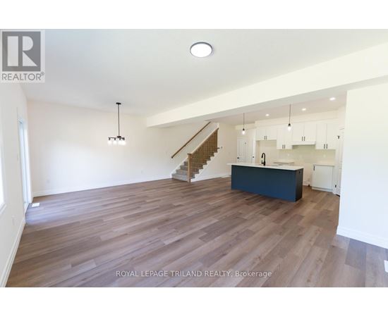 A spacious room with wooden flooring and a staircase leading to the upper level.