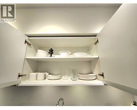 A white kitchen cabinet with plates and glasses on the shelf.