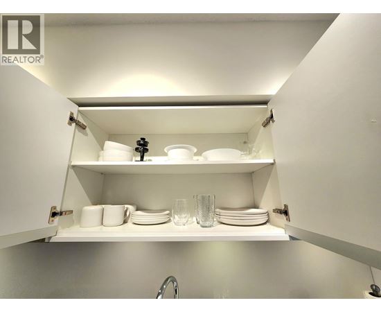 A white kitchen cabinet with plates and glasses on the shelf.