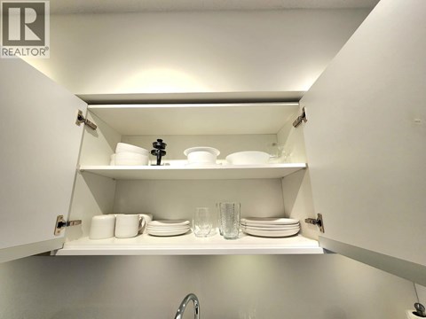 A white kitchen cabinet with plates and glasses on the shelf.