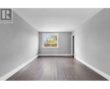 A spacious room with wooden flooring and a window showing a tree outside.