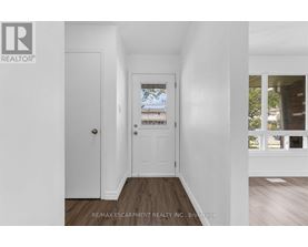 A hallway with a white door and a window with a view of a building and trees.