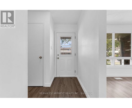 A hallway with a white door and a window with a view of a building and trees.