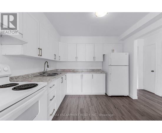 A white kitchen with a stove top oven and a refrigerator.