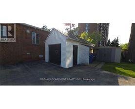 A small white building with a black door is in front of a brick building with a RE/MAX Escarpment Realty Inc. sign.