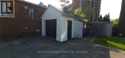 A small white building with a black door is in front of a brick building with a RE/MAX Escarpment Realty Inc. sign.