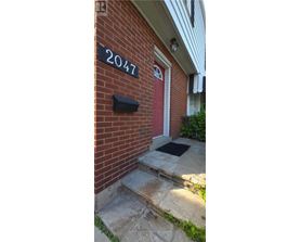 A red door with a black mailbox on a brick house with a number 2047 on the wall.