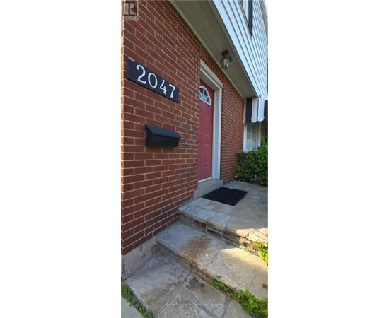 A red door with a black mailbox on a brick house with a number 2047 on the wall.