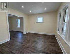 A room with wooden flooring and two windows.